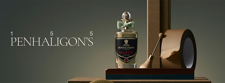 Penhaligon’s Duft 'Halfeti' mit dunklem Etikett und grüner Schleife steht auf einer minimalistischen Szenerie mit Packpapierrolle, Werkzeug und Holzrahmen. Links erscheint das elegante Penhaligon’s Logo mit '155'.