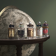 Fünf elegante Parfumflaschen aus der Trade Routes Kollektion von Penhaligon’s stehen auf einem Holztisch vor einem Globus. Jede Flasche hat einen runden silbernen Verschluss und individuelle Etiketten in verschiedenen Farben.