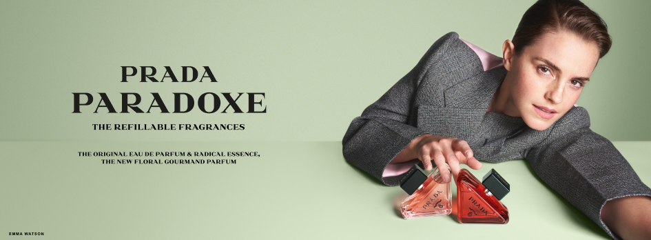 Werbebanner für den Duft Prada Paradoxe: Eine Person in grauem Outfit liegt nach vorne gelehnt und hält zwei dreieckige Parfümflakons in Rosa- und Orangetönen. Links steht der Schriftzug ‚Prada Paradoxe – The Refillable Fragrances‘ auf hellem grünlichem Hintergrund.